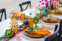 a colorful tropical boho wedding tablescape with colorful glasses, gold pineapples, gold candle lanterns and super bright blooms