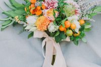 a colorful wedding bouquet of pink and orange blooms, greenery and leaves, kumquats and creamy ribbons for a chic look