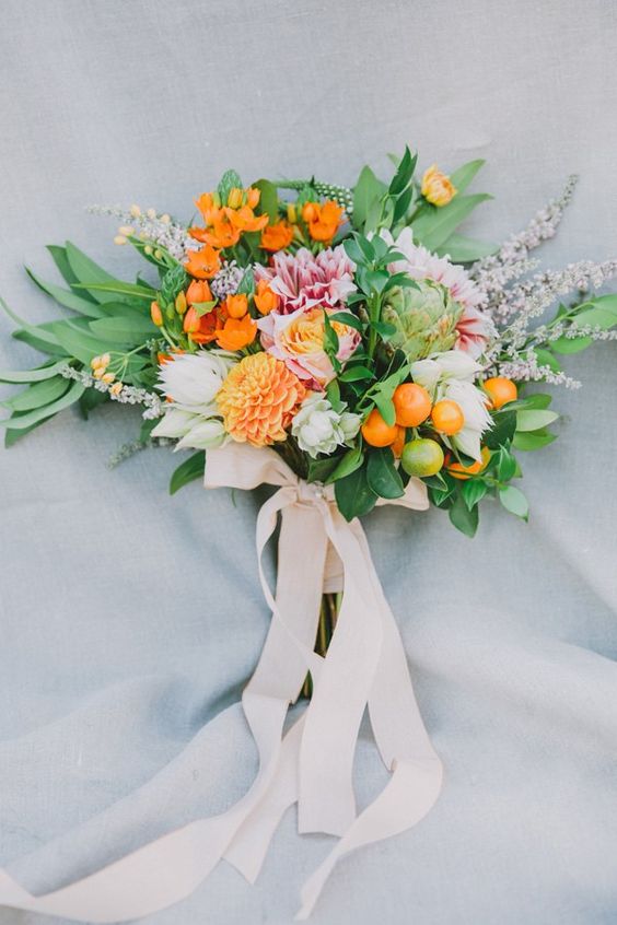a colorful wedding bouquet of pink and orange blooms, greenery and leaves, kumquats and creamy ribbons for a chic look