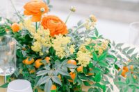 a colorful wedding centerpiece of greeneyr, yellow berries, orange blooms and kumquats is a lovely solution for a spring or summer wedding