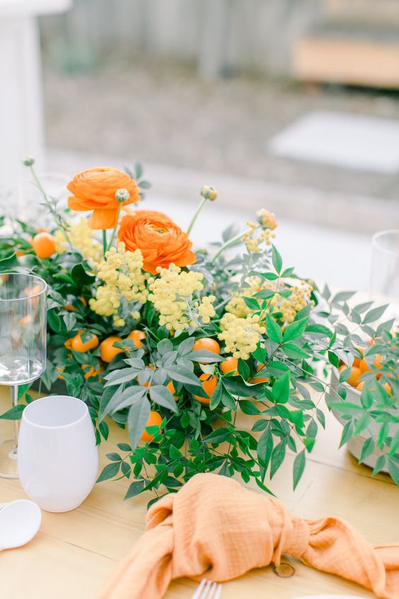 a colorful wedding centerpiece of greeneyr, yellow berries, orange blooms and kumquats is a lovely solution for a spring or summer wedding