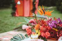 a colorful wedding table with tropical leaves and gold blooms in a bowl, with pink stationery and simple cutlery