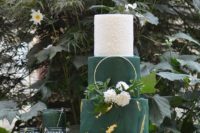 a dark green and white wedding cake with gold leaf, a textural white tier and some fresh blooms and a gold ring