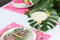 a glam tropical summer wedding tablescape with pink placemats, bright blooms and leaves and acrylic menus