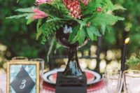a gorgeous wedding centerpiece of a black vase, ferns, pink blooms and a pink pineapple is a lovely and bright idea