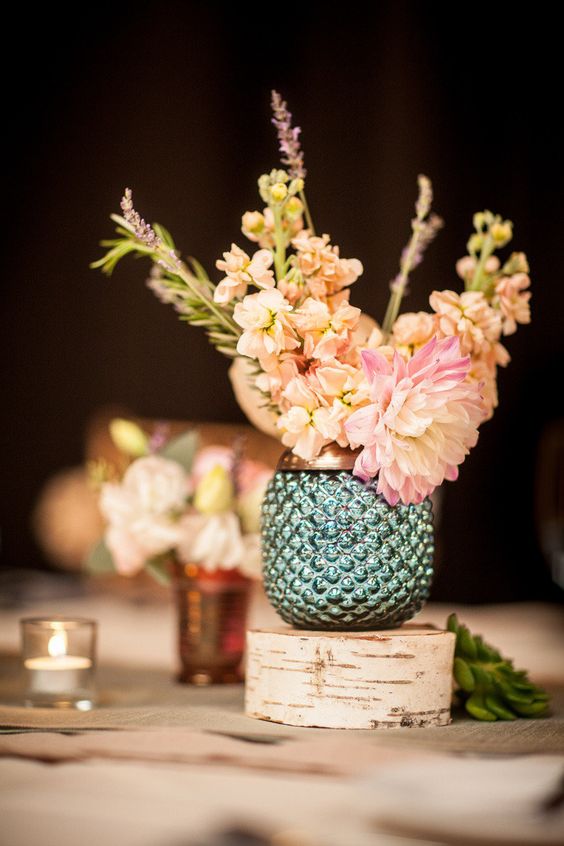 a green pineapple-shaped vase with pastel blooms and a wood slice under it for a lovely wedding centerpiece