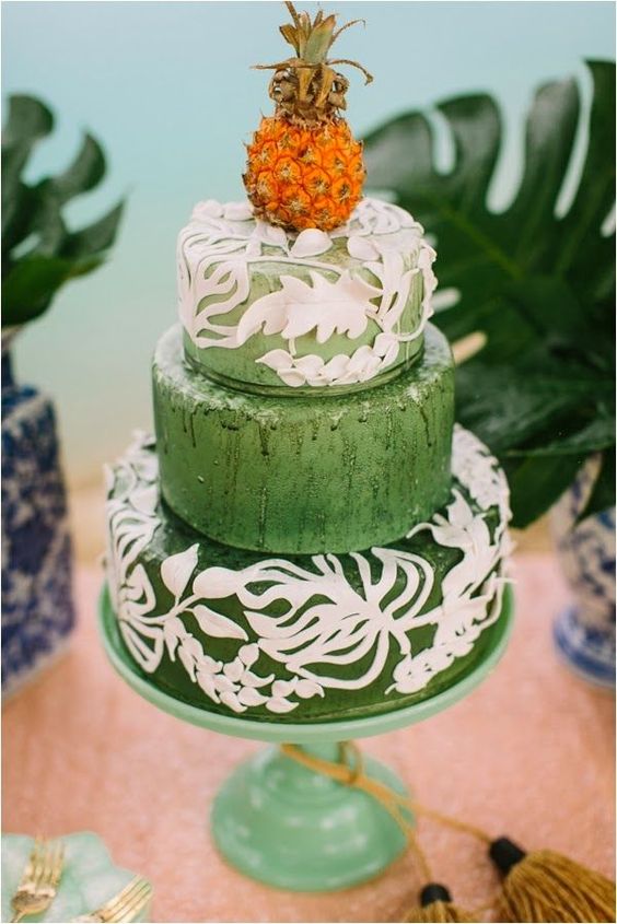 a green wedding cake with white leaf patterns and a mini pineapple on top for a bright tropical wedding