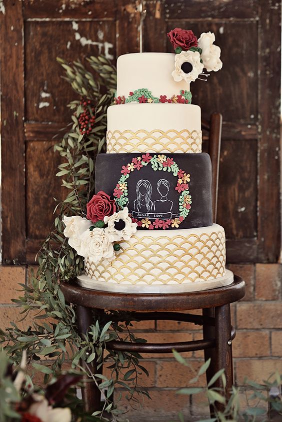 a large wedding cake with white and gold scallop tiers, with a chalkboard one, with portraits and sugar blooms in red and white