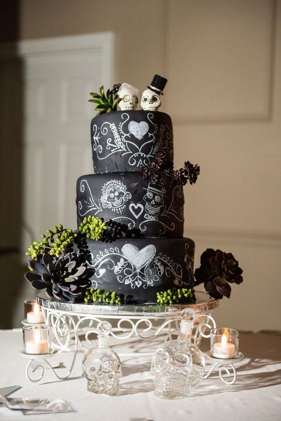 a lovely Halloween chalkboard wedding cake with creative chalking, with little sugar skulls, succulents and some candles around is amazing