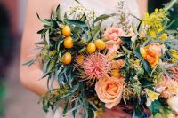 a lush and textural wedding arrangement of lots of greenery, herbs, bold blooms and blooming branches and kumquats plus blue ribbon