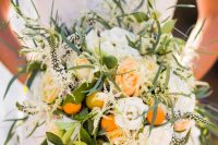 a lush and textural wedding bouquet of orange and white roses, kumquats, feathers, greenery, blooming branches is gorgeous