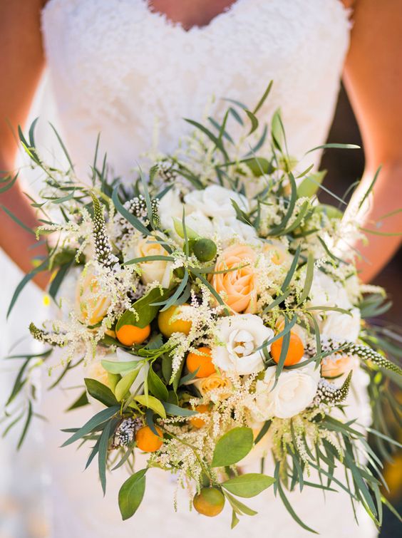 a lush and textural wedding bouquet of orange and white roses, kumquats, feathers, greenery, blooming branches is gorgeous