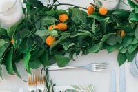 a lush wedding table runner of greenery and leaves and kumquats, with pillar candles is a gorgeous bright idea for a wedding