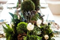 a lush woodland wedding centerpiece of moss, greenery, succulents, pinecones and white blooms plus candles