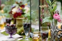 a luxurious woodland wedding tablescape with a moss runner, blooms, berries, feathers and candle lanterns