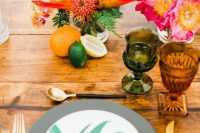 a modern bold tropical wedding table with colored glasses, tropical leaf plates, colorful blooms and fruits