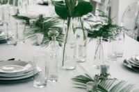 a modern tropical wedding tablescape with ferns and fronds, white porcelain and clear glass