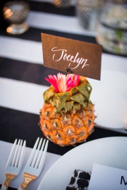 a pineapple topped with a pink flower and a card is a lovely table accent idea for a modern tropical wedding table
