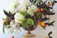 a pretty wedding centerpiece with white ranunculus and other blooms, greenery and kumquats is a lovely idea for the summer