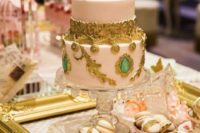 a refined blush wedding cake with gold detailing and green rhinestones is a very sophisticated idea
