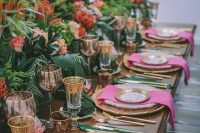a refined tropical wedding tablescape with greenery, leaves and bold blooms, pink napkins and gold cutlery, gold rim glasses and plates