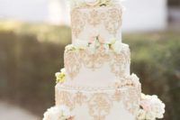 a refined white wedding cake with gold patterns and fresh white blooms and greenery on top