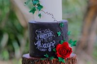 a rustic chalkboard, tree stump and white wedding cake topped with red roses and greenery for a rustic or woodland wedding