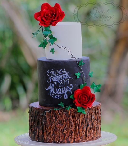 a rustic chalkboard, tree stump and white wedding cake topped with red roses and greenery for a rustic or woodland wedding
