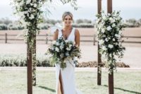 a rustic wedding arch decorated with greenery and white blooms is a cool idea for a modern wedding