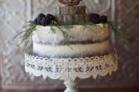 a semi naked chocolate wedding cake topped with greenery, berries, wood slices and a chalkboard topper