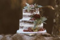 a semi naked wedding cake topped with fresh eucalyptus and roses and with berries for a forest wedding