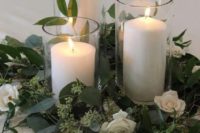 a simple wedding centerpiece of greenery, white blooms and white pillar candles will fit many wedding styles