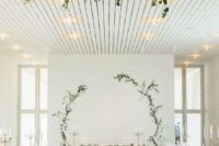 a simple white wall with greenery branches to form a circle is a cool idea, add a matching chandelier