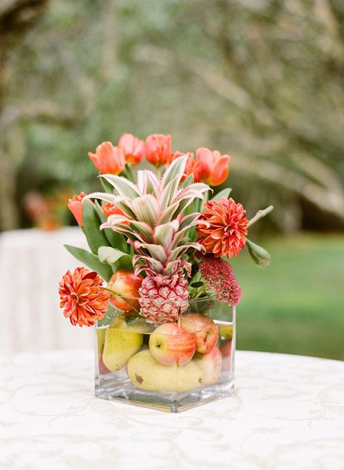 a square glass vase with apples, pears, bold blooms and a pink pineapple is a lovely and easy bright wedding centerpiece