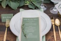 a stylish wedding tablescape done in green, gold and white, with a leafy runner and a green and copper menu