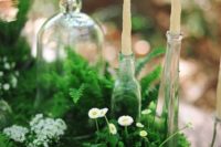 a summer woodland wedding centerpiece of lush greenery, white blooms and candles in glass bottles