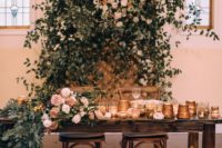 a super lush greenery and blush blooms reception backdrop plus a table runner and lots of candles
