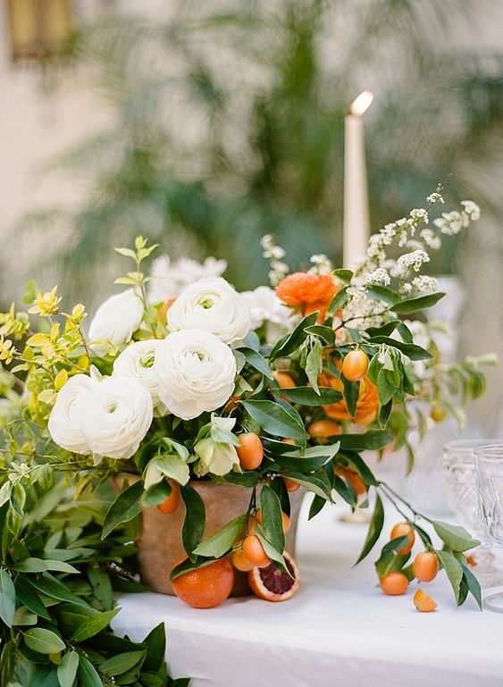 a terracotta pot with greenery, with blooming branches, kumquats, white ranunculus, citrus for a wedding centerpiece