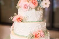 a vintage-inspired white wedding cake with patterns, pink blooms and baby’s breath and a metallic monogram