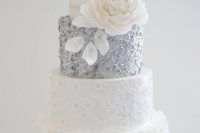 a white and silver wedding cake with textural and patterned tiers, an oversized white sugar bloom is very refined