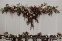 a white curtain backdrop with lush greenery and bright blooms on top plus matching florals on the tables