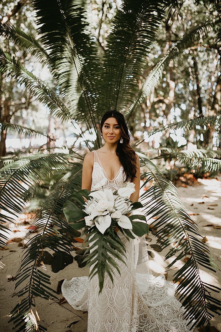 a white lace wedding dress with a deep neckline, no sleeves and a long train is an adorable idea for a tropical boho wedding