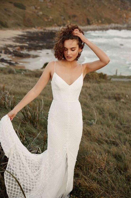 a white sheath textural wedding dress with a V-neckline, a front slit, spaghetti straps and a train for a modern bride