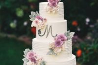 a white textural wedding cake with a monogram and neutral and purple blooms and foliage of sugar