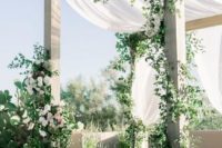 a white wedding arch with curtainsm greenery and white blooms looks luxurious