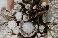 a white wedding bouquet of king proteas, white roses, berries, magnolia leaves and pale greenery