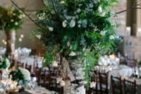 a woodland wedding centerpiece of a tree stump, white blooms, greenery and candle holders hanging on branches