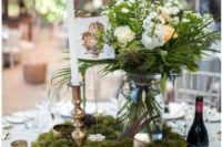 a woodland wedding centerpiece of a wood slice, moss, blooms and greenery in a jar, feathers and candles