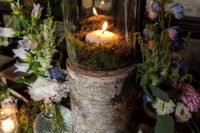 a woodland wedding centerpiece of bold blooms, greenery, moss and a tree stump with a candle and moss