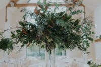 a woodland wedding centerpiece with a tall clear vase and lots of textural greenery and foliage